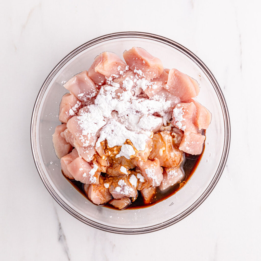 cubed raw chicken in glass bowl with flour and seasoning