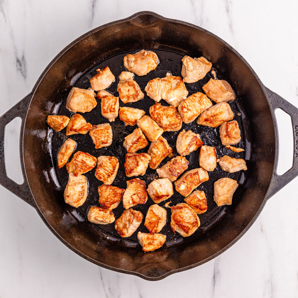 browning cubed chicken in cast iron skillet for black pepper chicken