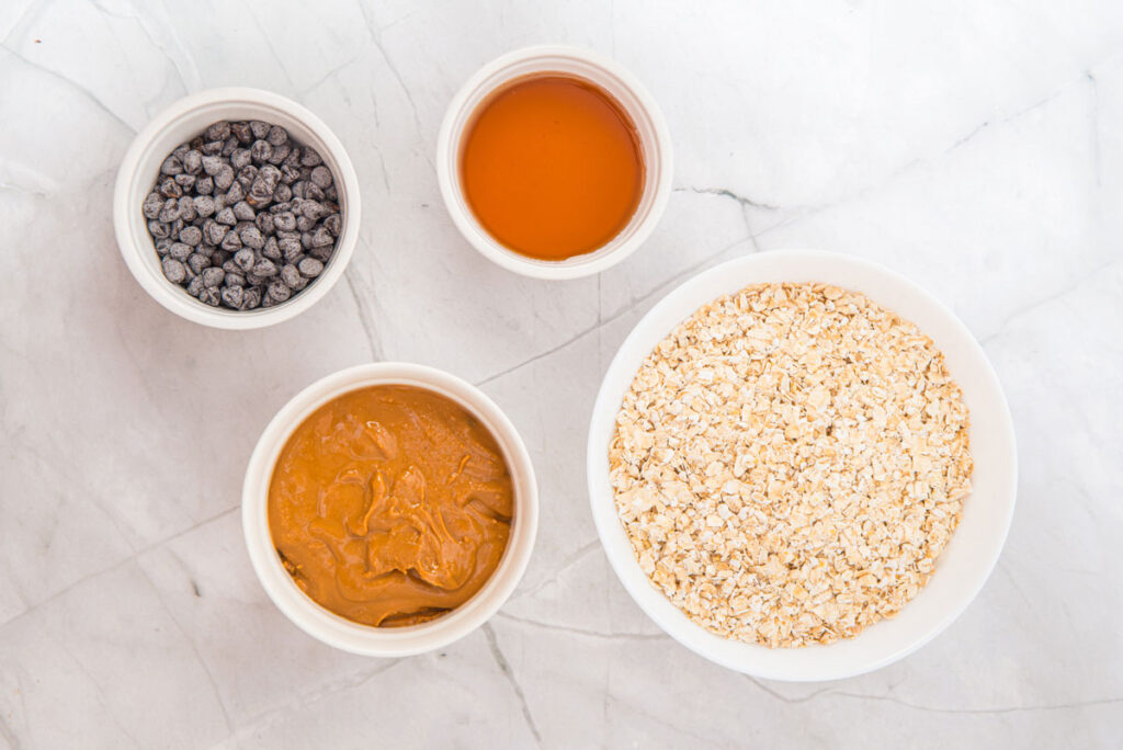 peanut butter oatmeal balls ingredients in white bowls on marble countertop