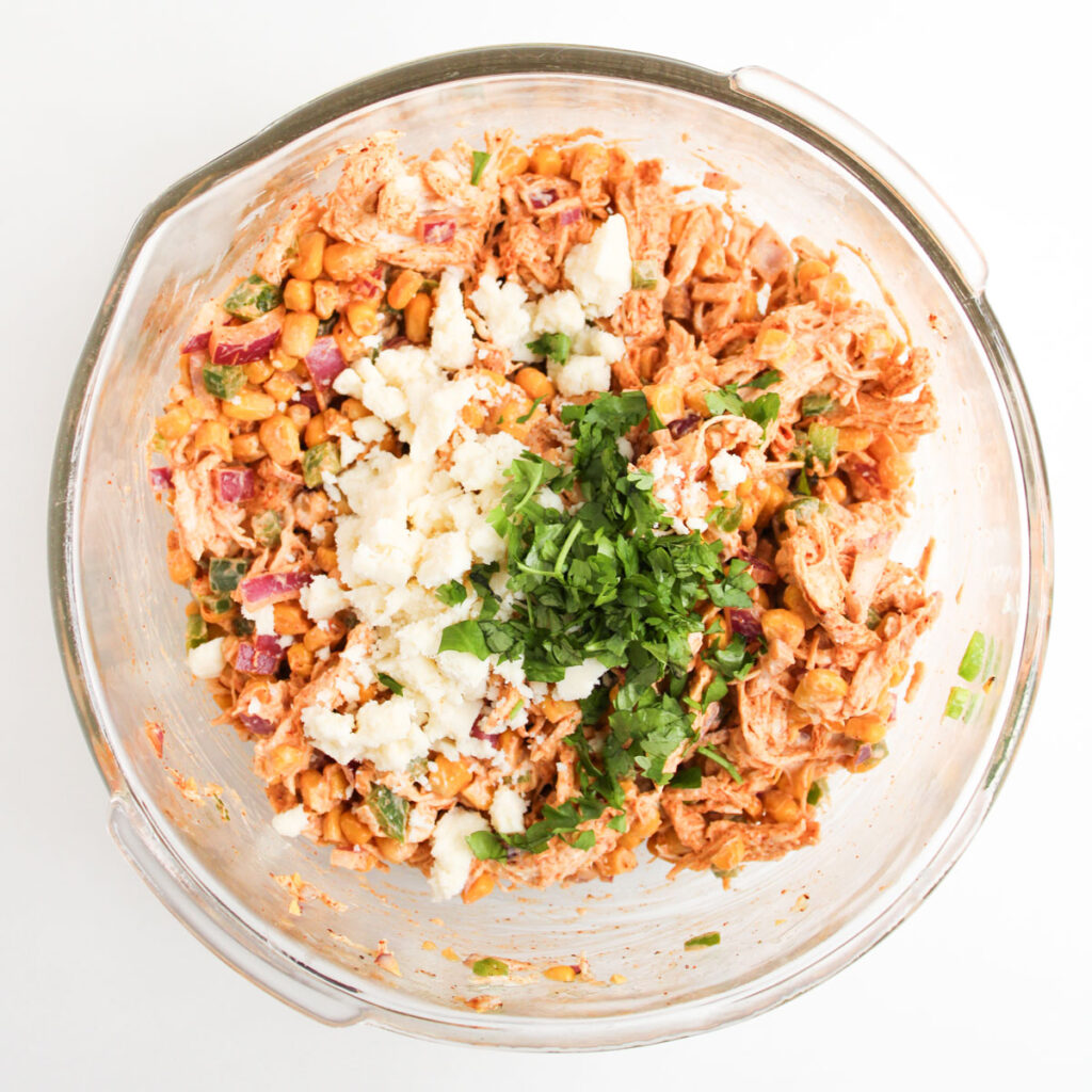 adding onion and cilantro to street corn chicken salad