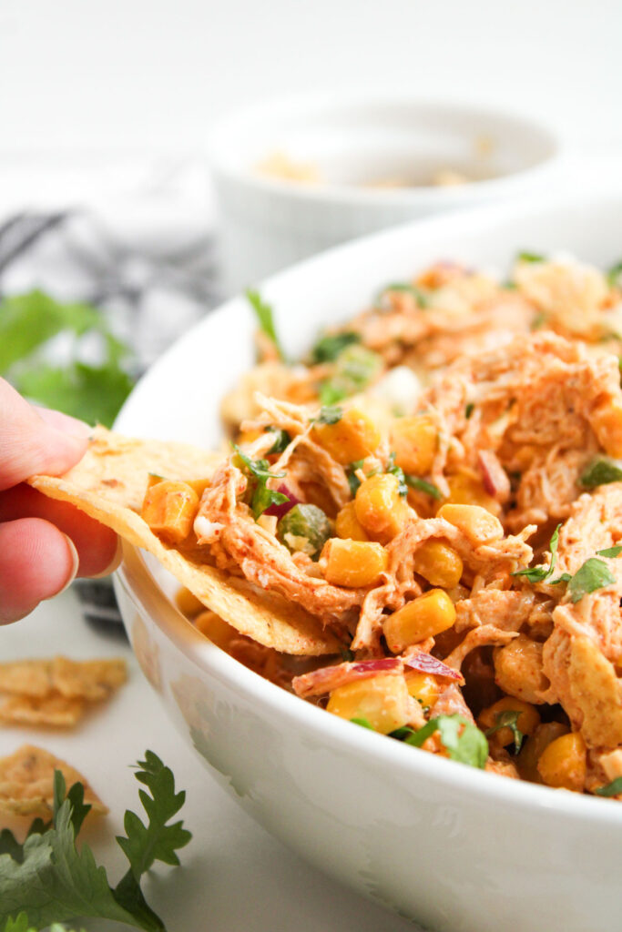 chip scooping street corn chicken salad from white bowl