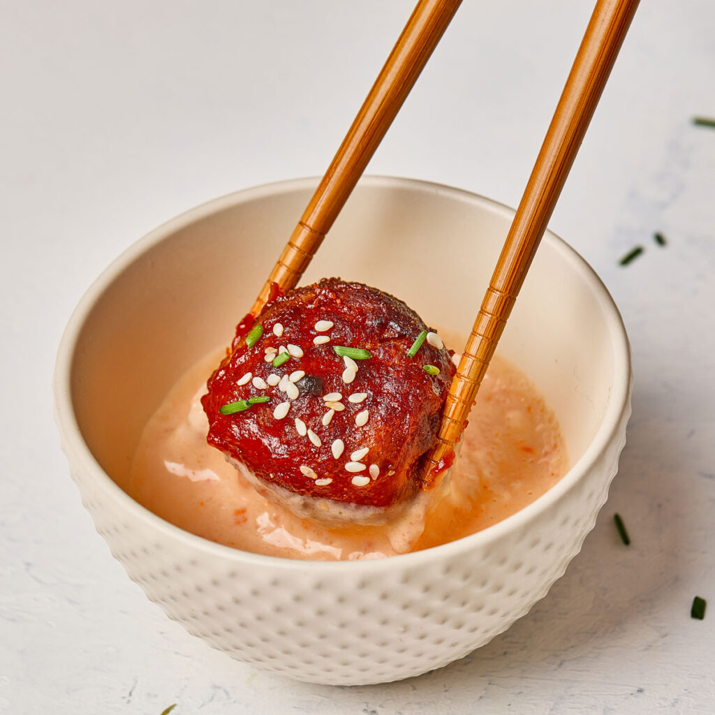 chopsticks dipping korean meatball in dipping sauce