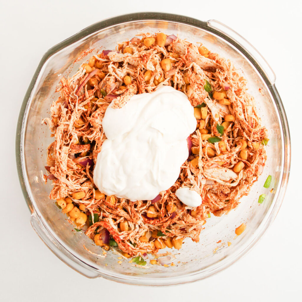 adding dressing to street corn chicken salad in glass bowl