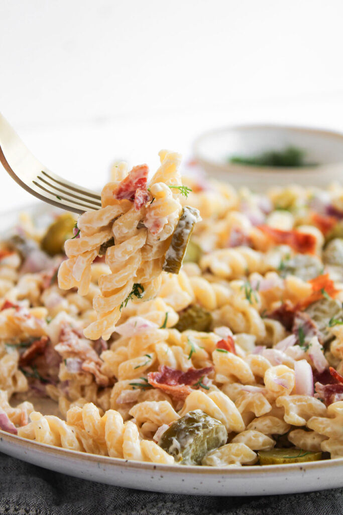 fork picking up bite of pickle pasta salad over plate